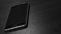 Black smartphone placed on a dark wooden table, showcasing modern design. (Foto: Erkan Utu / Pexels)