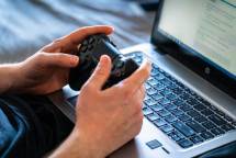 Person holds a gaming controller while interacting with a laptop, emphasizing modern gaming technology. (Foto: Castorly Stock / Pexels)