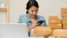 Wanita memeriksa paket pesanan online dengan smartphone di samping laptop dan kardus e-commerce (Foto: Unsplash)